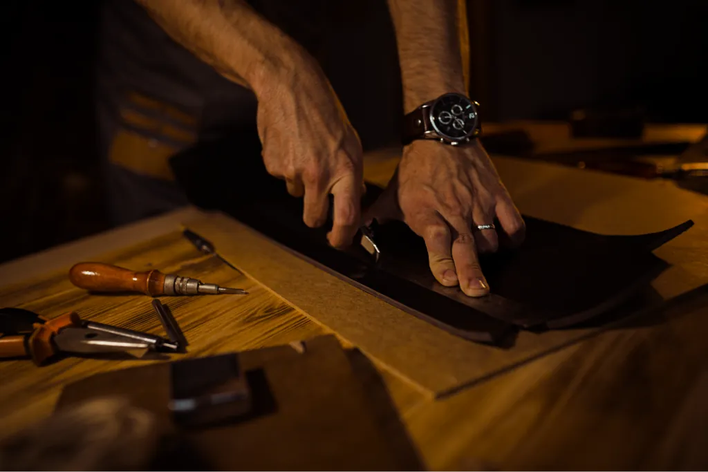 An artisan hand-stitching a leather panel at a workbench